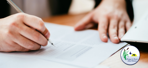 &quot;Close-up of a male hand holding a pen and writing on a sheet of paper placed on a wooden table, with natural light illuminating the workspace.&quot;